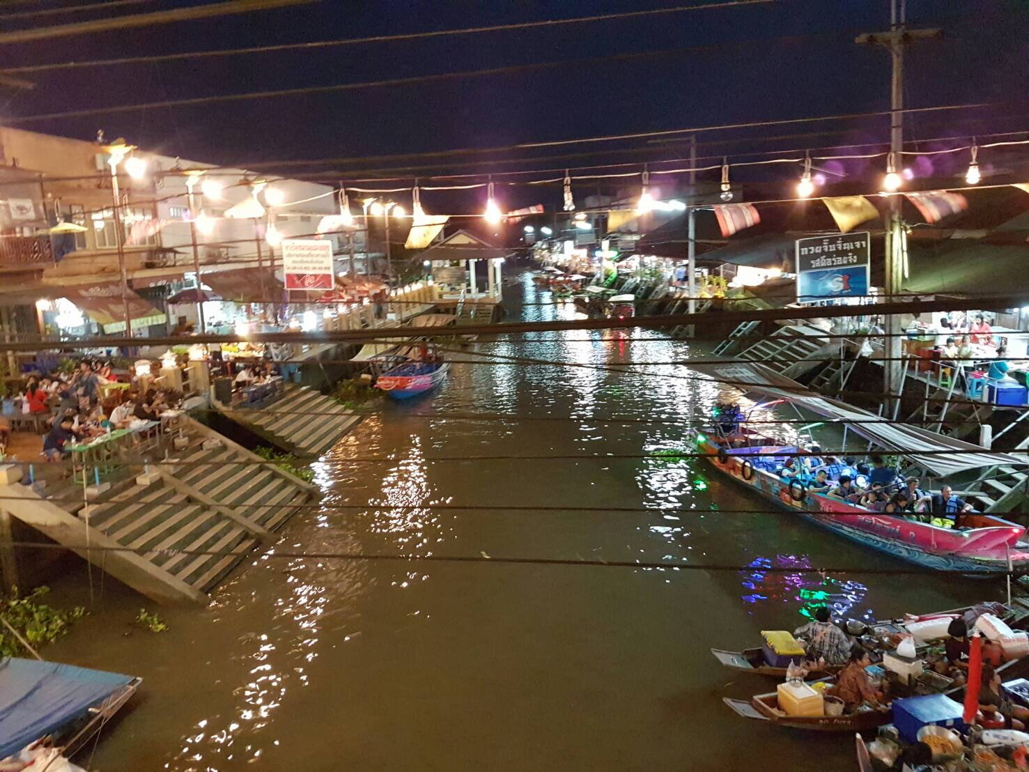 Boats and lit timber shophouses along the canal at Amphawa after dark