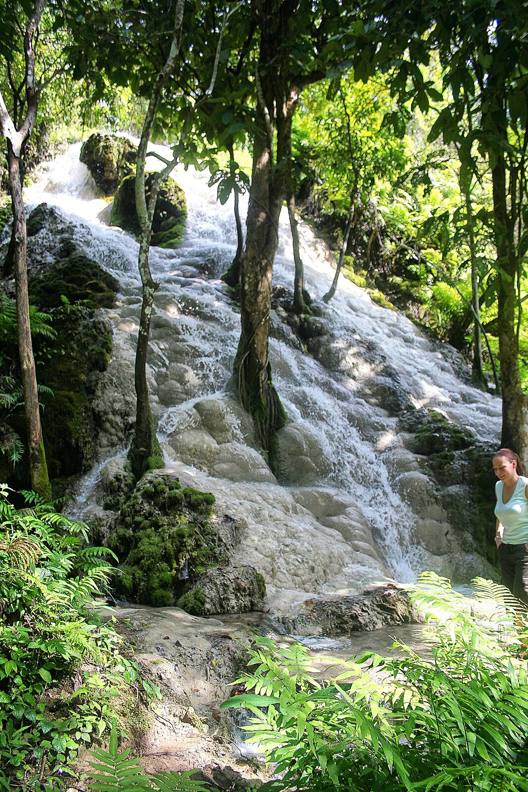 Water cascading over pale limestone terraces at Bua Thong, a visitor standing at the base