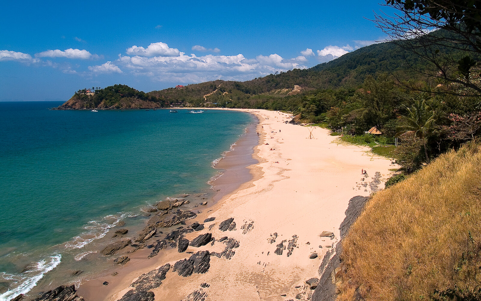 A curving white-sand beach and turquoise bay seen from a wooded headland, Koh Lanta