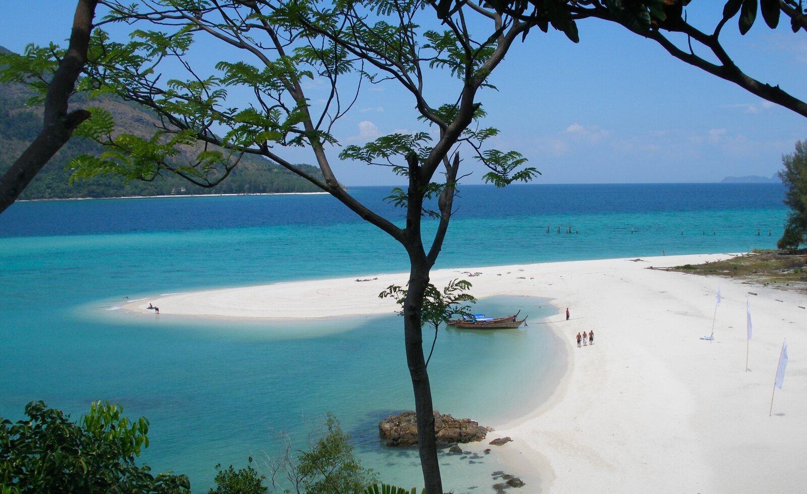 A sandbar curling into pale turquoise shallows with a longtail boat, Koh Lipe