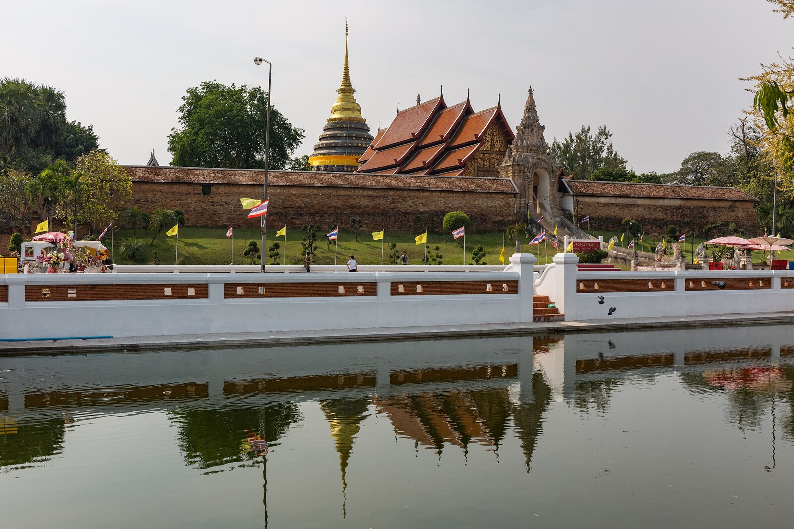 Wat Phra That Lampang Luang's gold chedi and red roofs reflected in a still moat