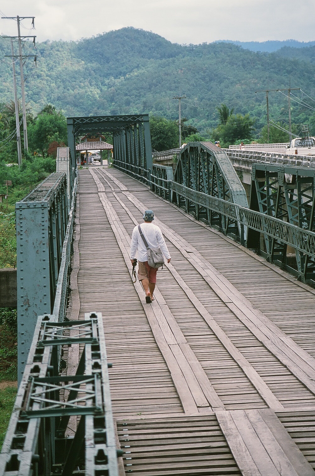 A walker crossing the old iron memorial bridge over misted hills, Pai