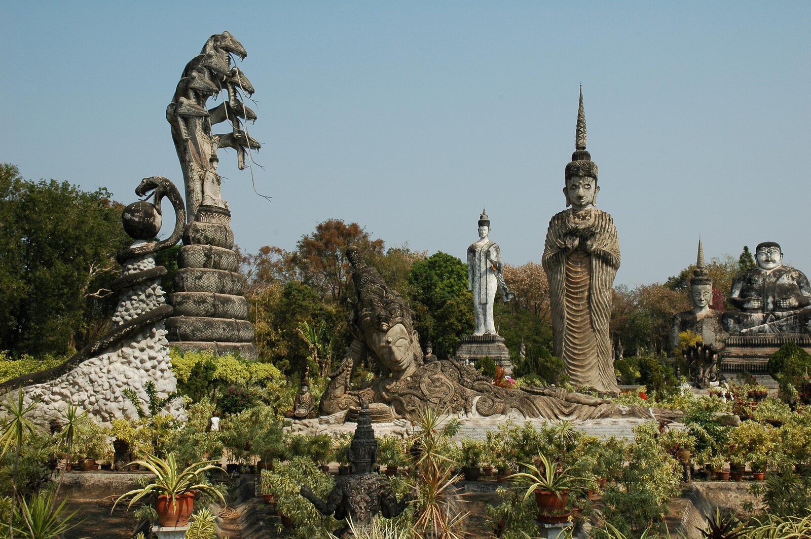 A towering multi-headed naga statue beside standing Buddha figures at Sala Keoku