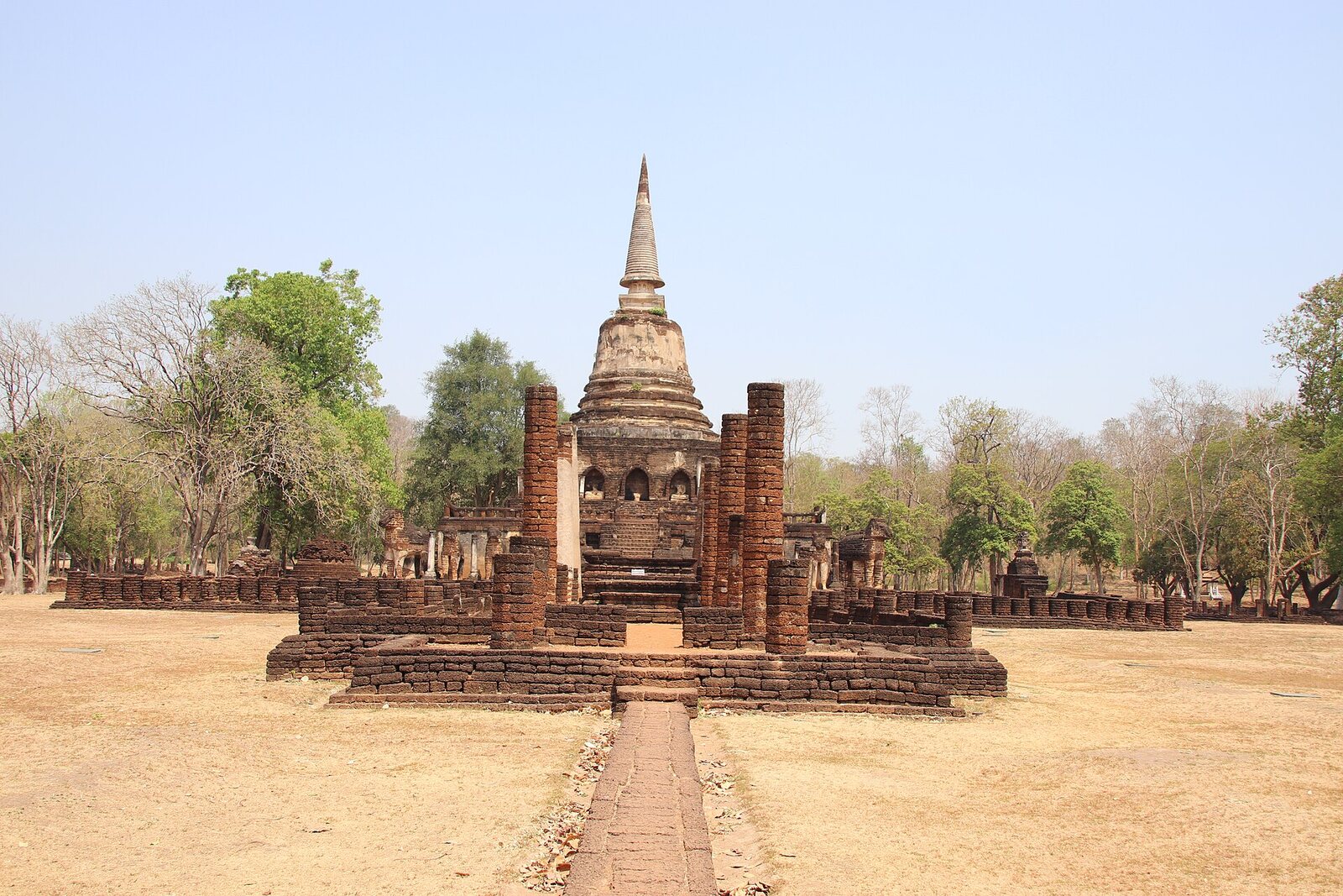 A weathered bell-shaped brick chedi with niched Buddhas amid the ruins at Si Satchanalai