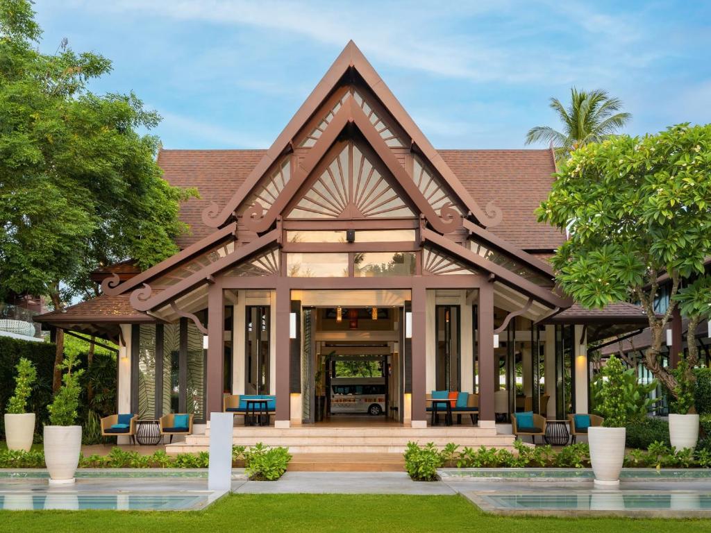The resort's open-sided Thai pavilion entrance with a steep tiled roof and carved gable, rattan lounge seating either side and a garden path leading in from the pool.