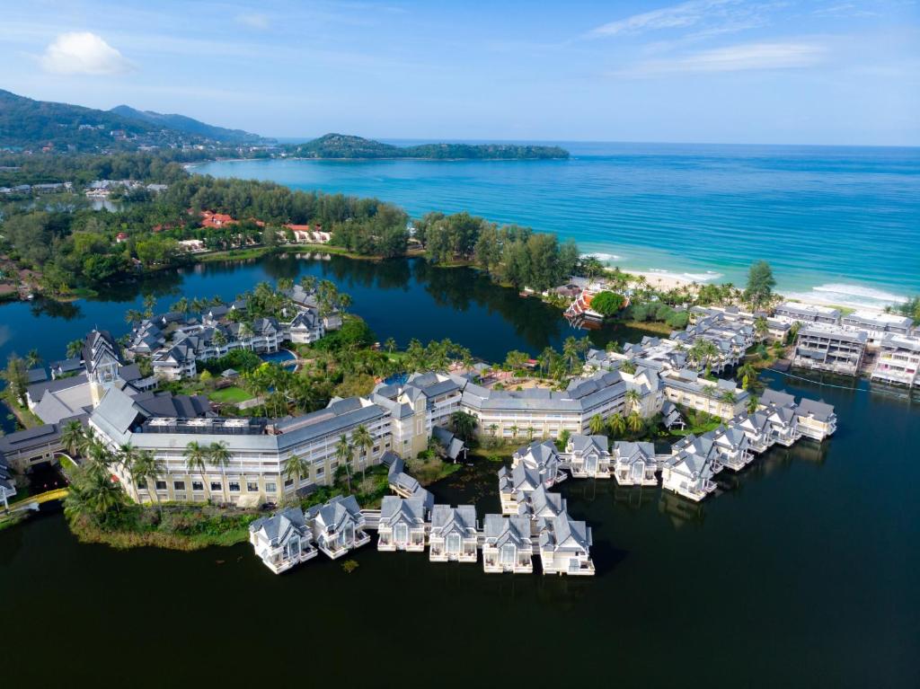 An aerial view of the Laguna Phuket estate's canal-side villas and water bungalows arranged around a lagoon, the beach and sea beyond a fringe of palms.