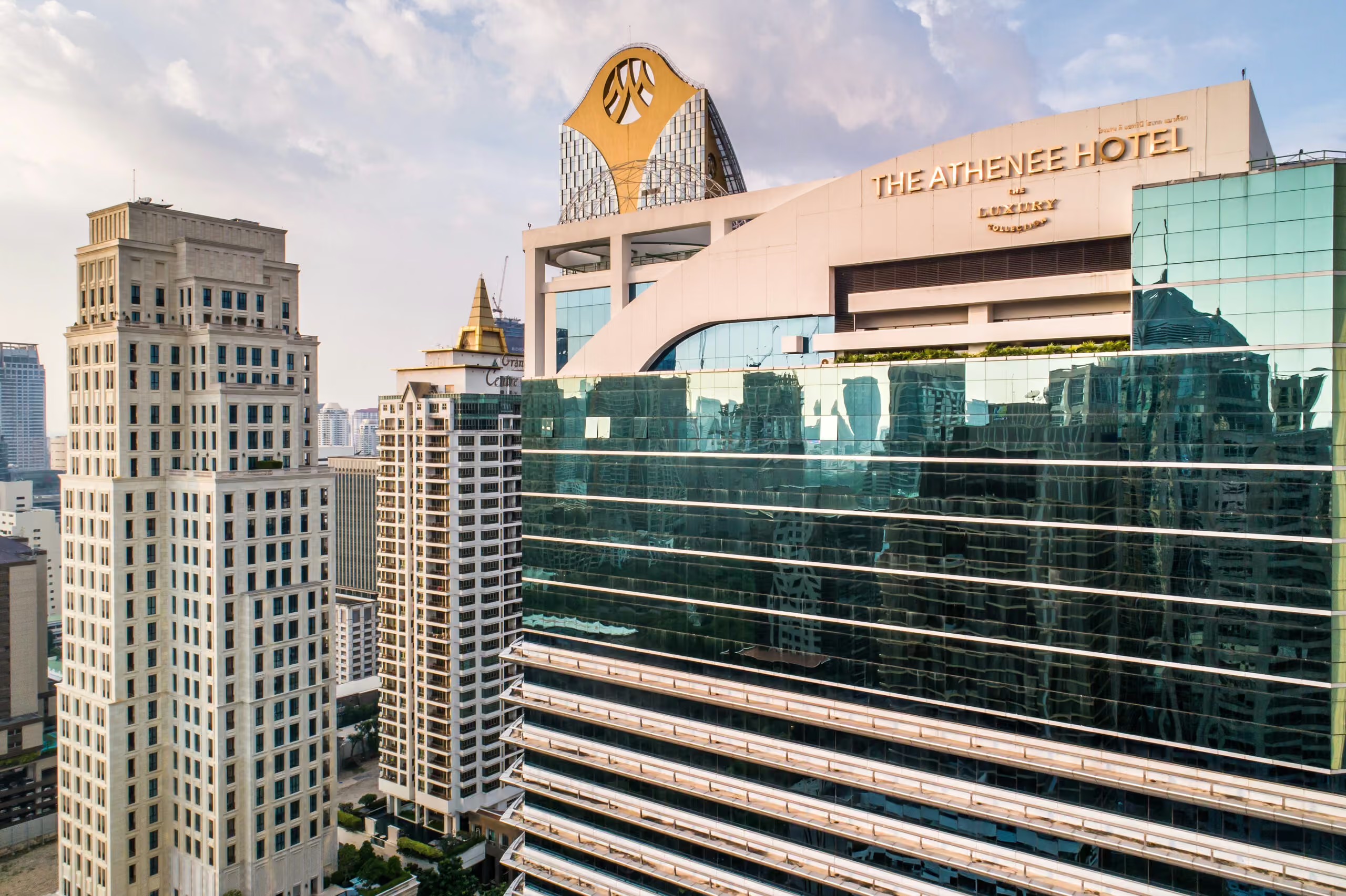 The hotel's glass tower in late-afternoon light, THE ATHENEE HOTEL lettering along the upper facade and neighbouring Ploenchit towers to the left.