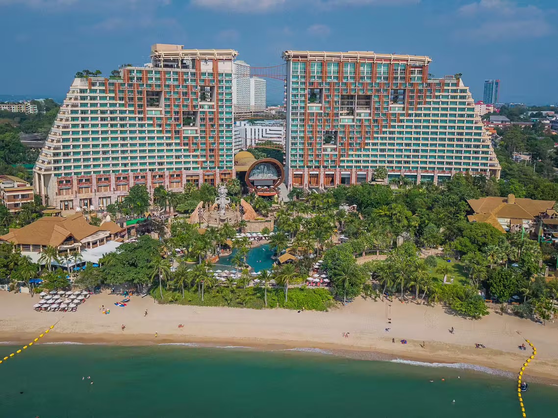 An aerial view of the resort's twin stepped pyramid towers linked by a sky bridge, a themed pool and gardens between them leading down to the beach.