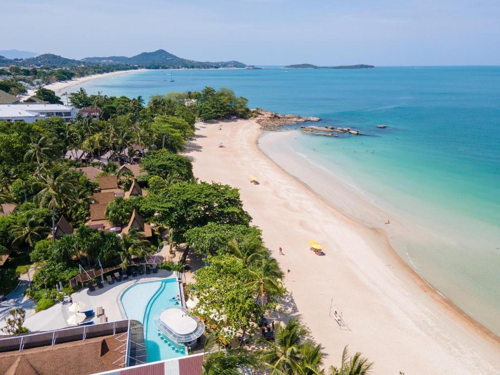 An aerial view of the resort's beachfront pool and low-rise pavilions set among palms, Chaweng's curving white-sand beach and turquoise water stretching beyond.