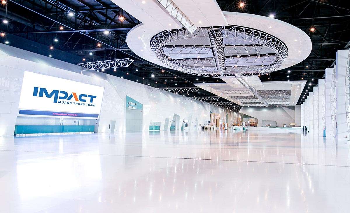 A vast white exhibition hall, empty and polished, an illuminated IMPACT Muang Thong Thani sign on the left-hand wall and a circular sculptural feature suspended from the ceiling.