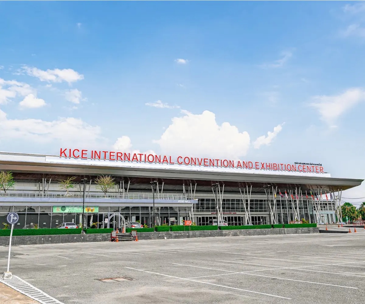 The building's long canopy roofline with red KICE INTERNATIONAL CONVENTION AND EXHIBITION CENTER lettering above a glazed facade and an empty forecourt car park.