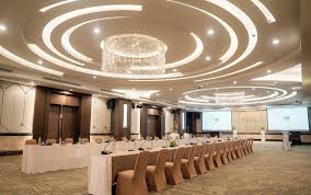 A ballroom set classroom-style with rows of pink-cushioned chairs facing a screen, twin ring-shaped crystal chandeliers suspended from a coved ceiling.