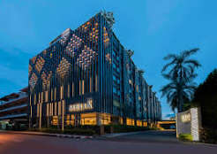 The hotel's facade at dusk, a perforated diamond-pattern metal screen lit from within across the upper storeys, a palm tree and the property sign at street level.