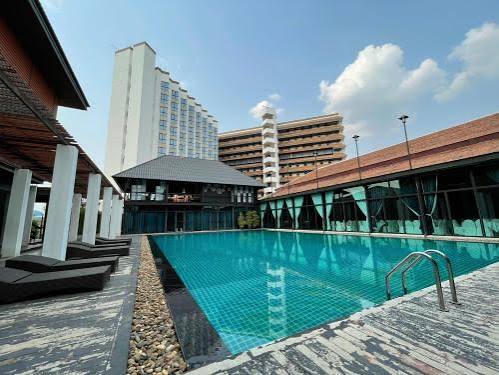 A long tiled swimming pool beside a two-storey pavilion with a peaked tile roof, sun loungers along one side and the hotel tower rising behind.