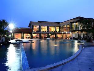 The hotel's dark timber and glass facade lit at dusk, reflected in a curved swimming pool with loungers along the near edge.