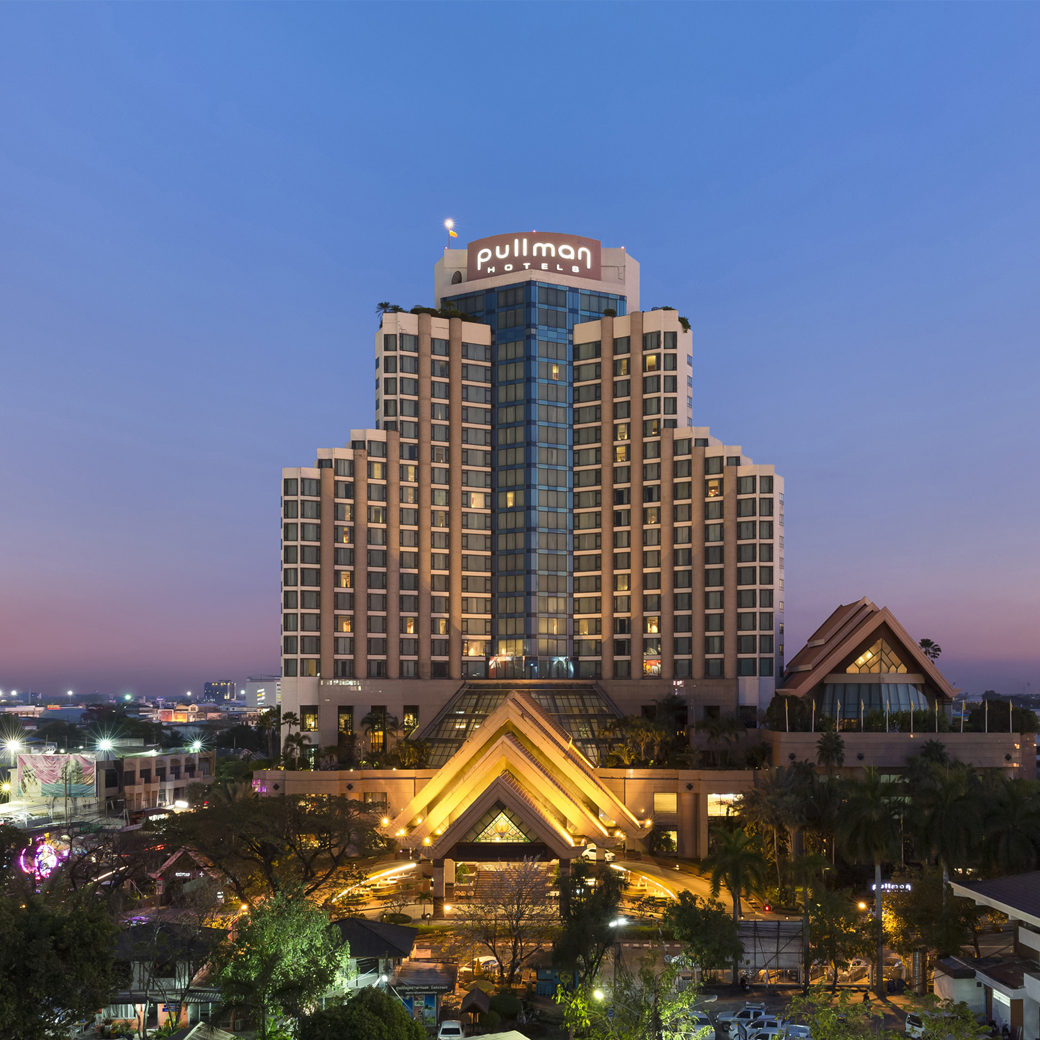 The hotel tower at dusk, illuminated pullman HOTELS signage at its crown, a lit triangular entrance canopy below.