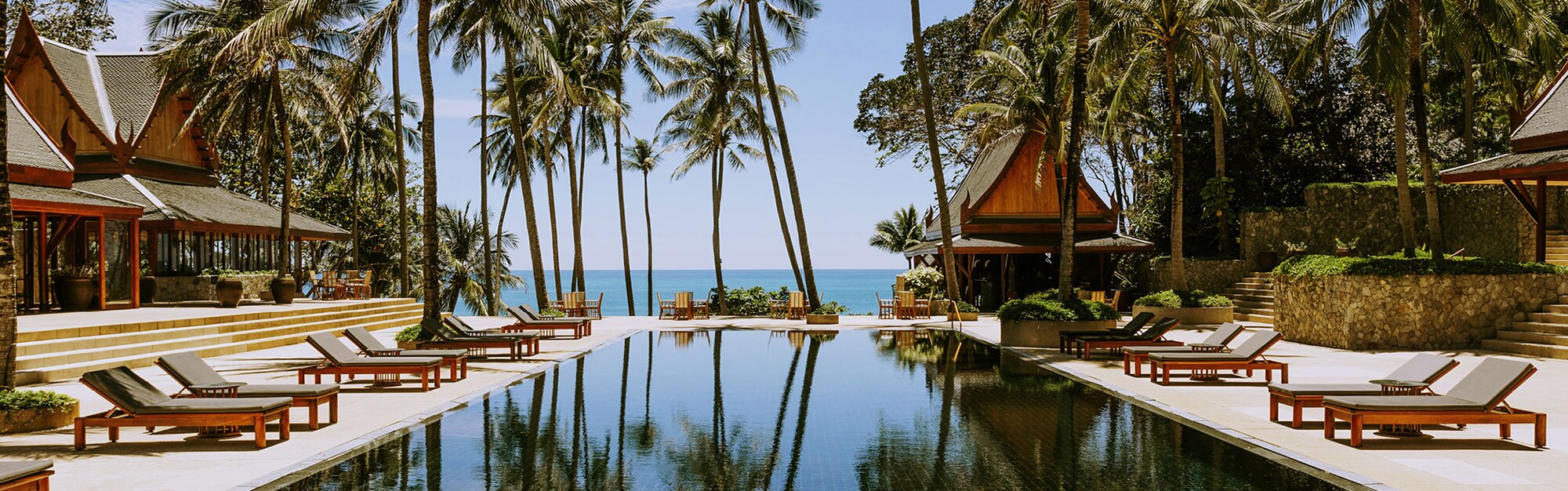 Amanpuri's black-tiled pool between Thai pavilions and coconut palms, the Andaman Sea beyond