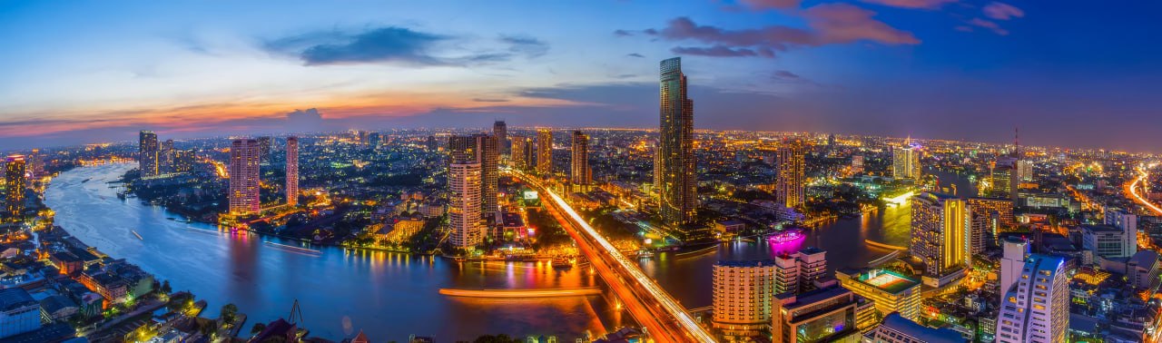 The Chao Phraya curving through Bangkok at dusk, the city lit along both banks