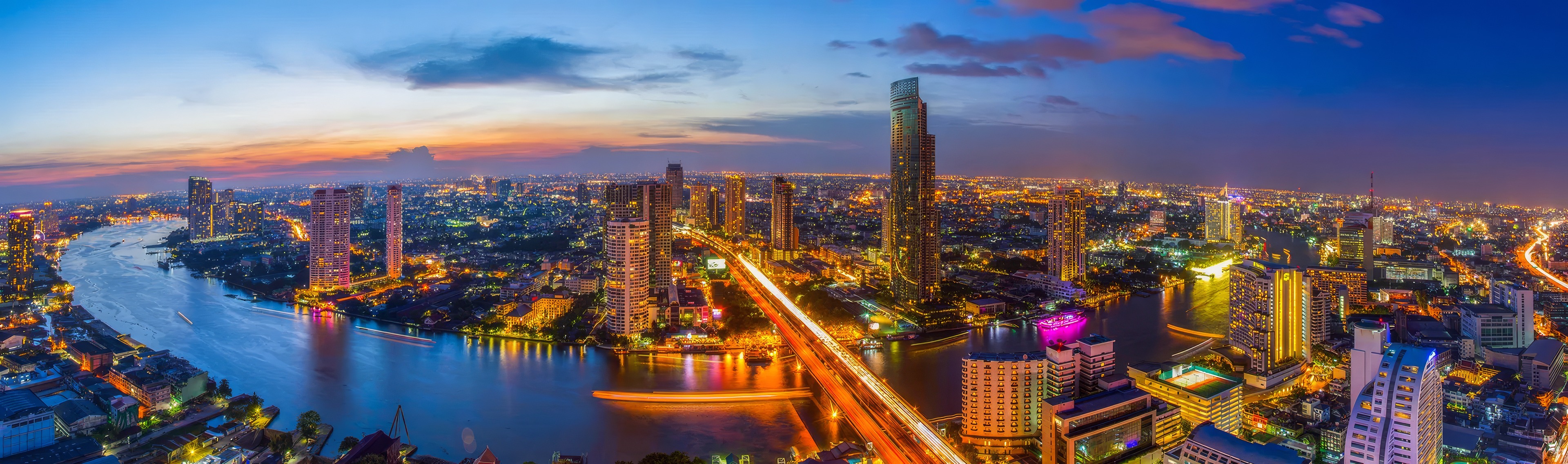 The Chao Phraya curving through Bangkok at dusk, the city lit beyond