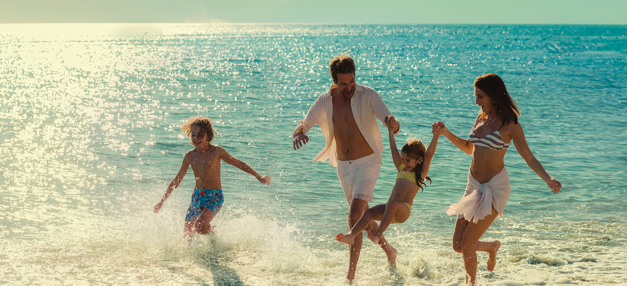 Two parents and two children running together through the shallows in late afternoon sun