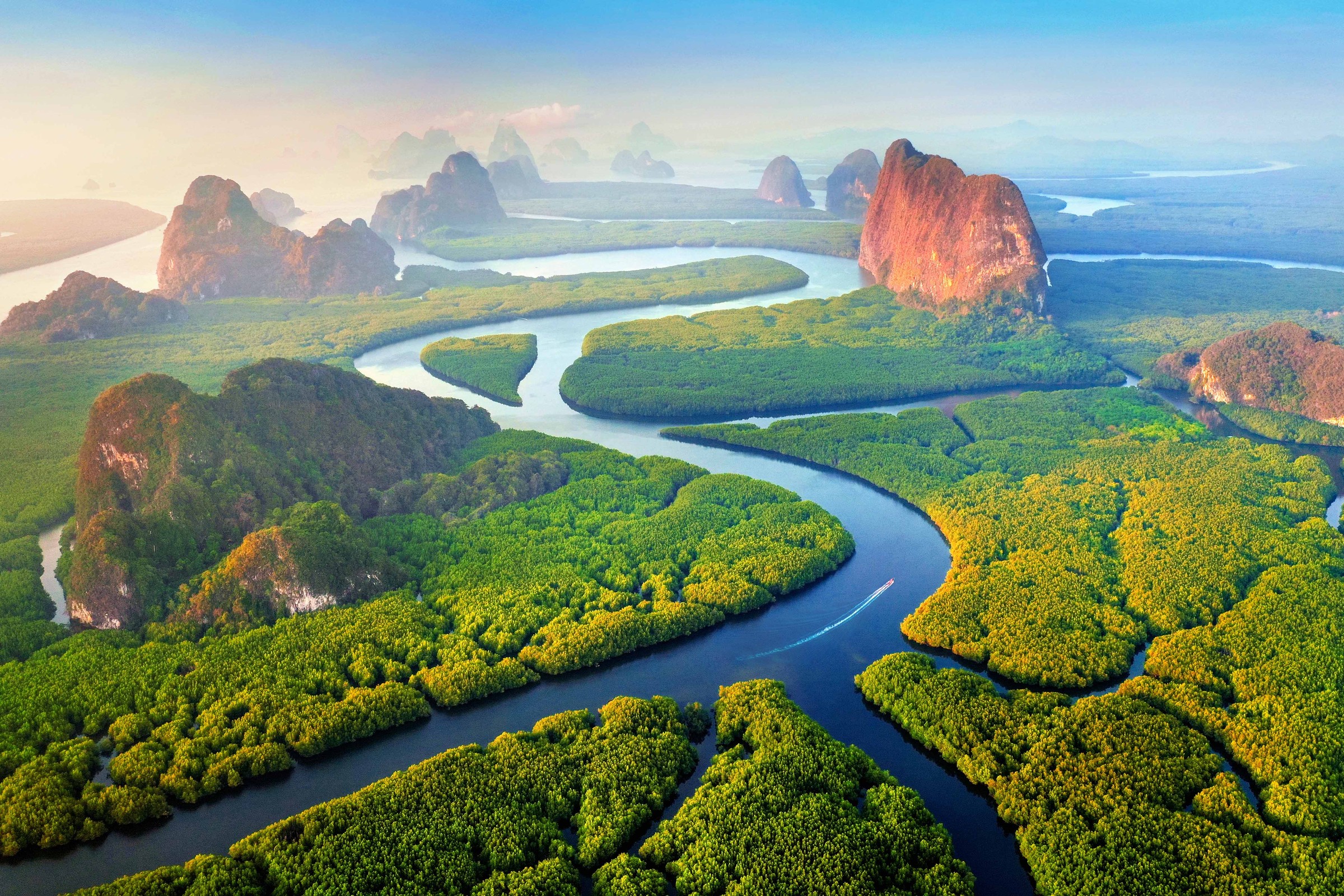 A river winding through mangrove forest beneath limestone karsts, seen from the air