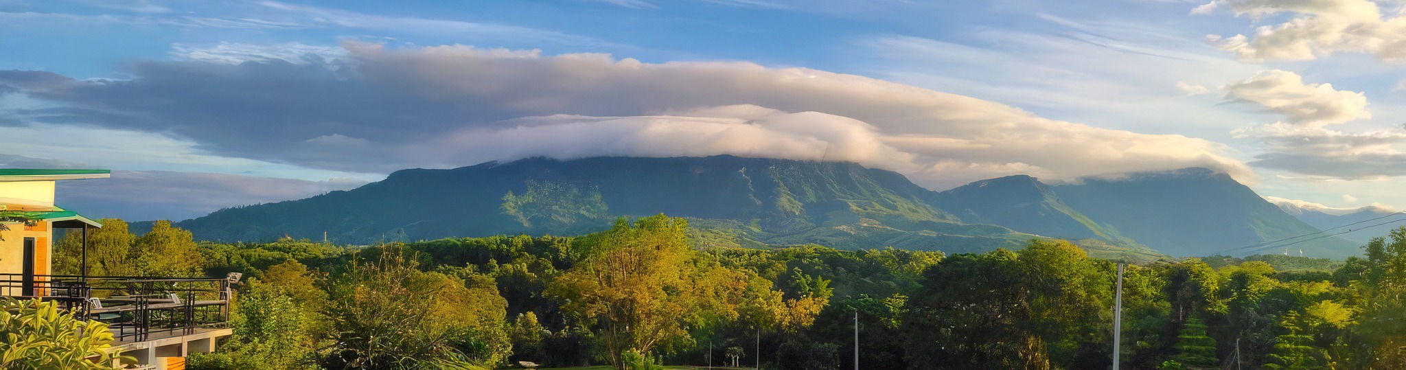 A mountain ridge under a cap of cloud above forested hills