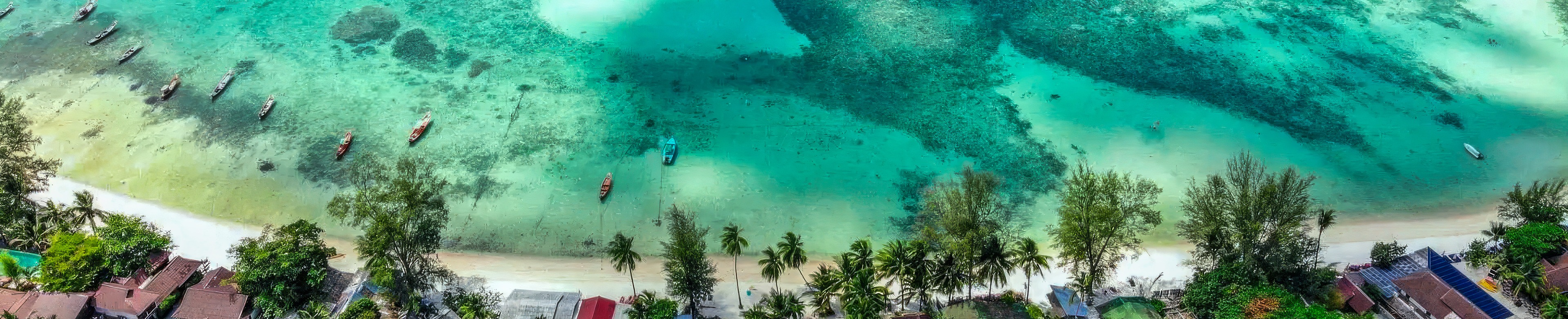 An aerial view of reef and shallows off a Koh Phangan beach, longtail boats at anchor