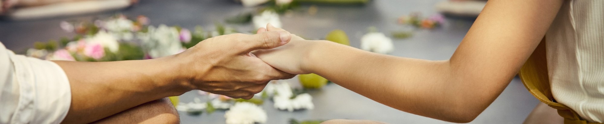 A therapist working on a guest's hand and wrist, flowers scattered on the mat