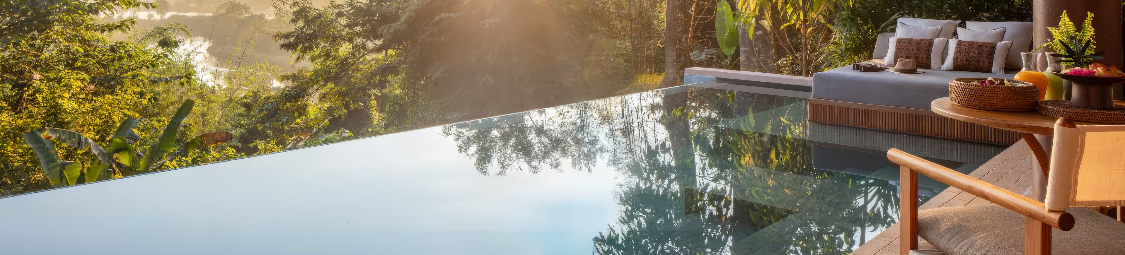 An infinity pool and daybed above forest in morning light