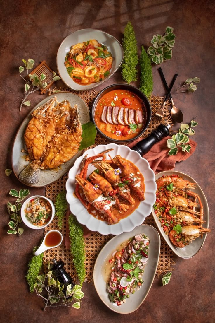A Thai table from above — whole fried fish, river prawns in curry, grilled prawns, larb and dips on rattan