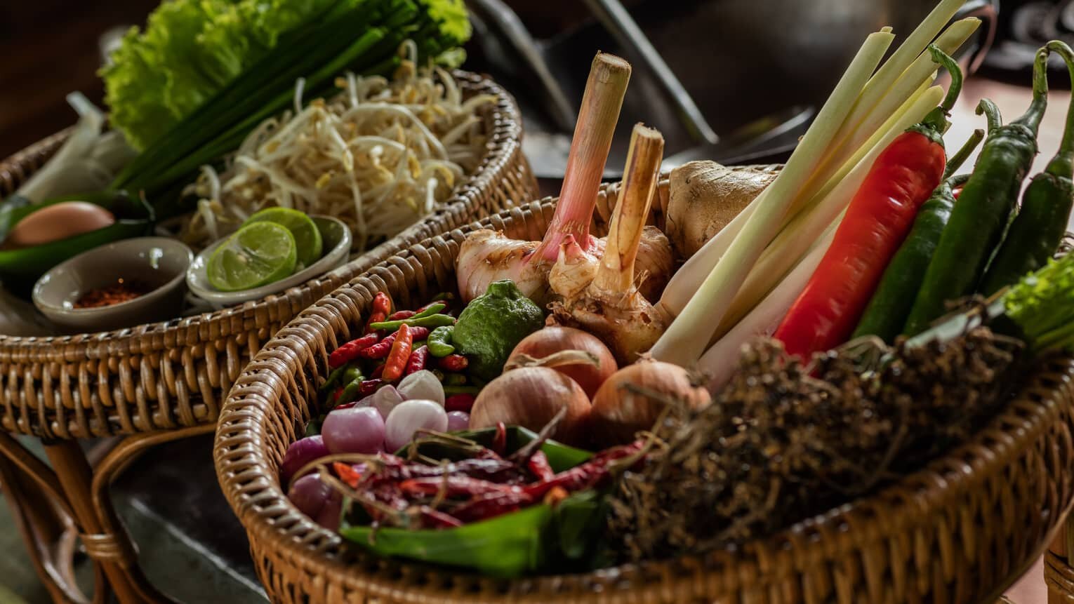 A basket of fresh curry paste ingredients — lemongrass, galangal, shallots, and chilies