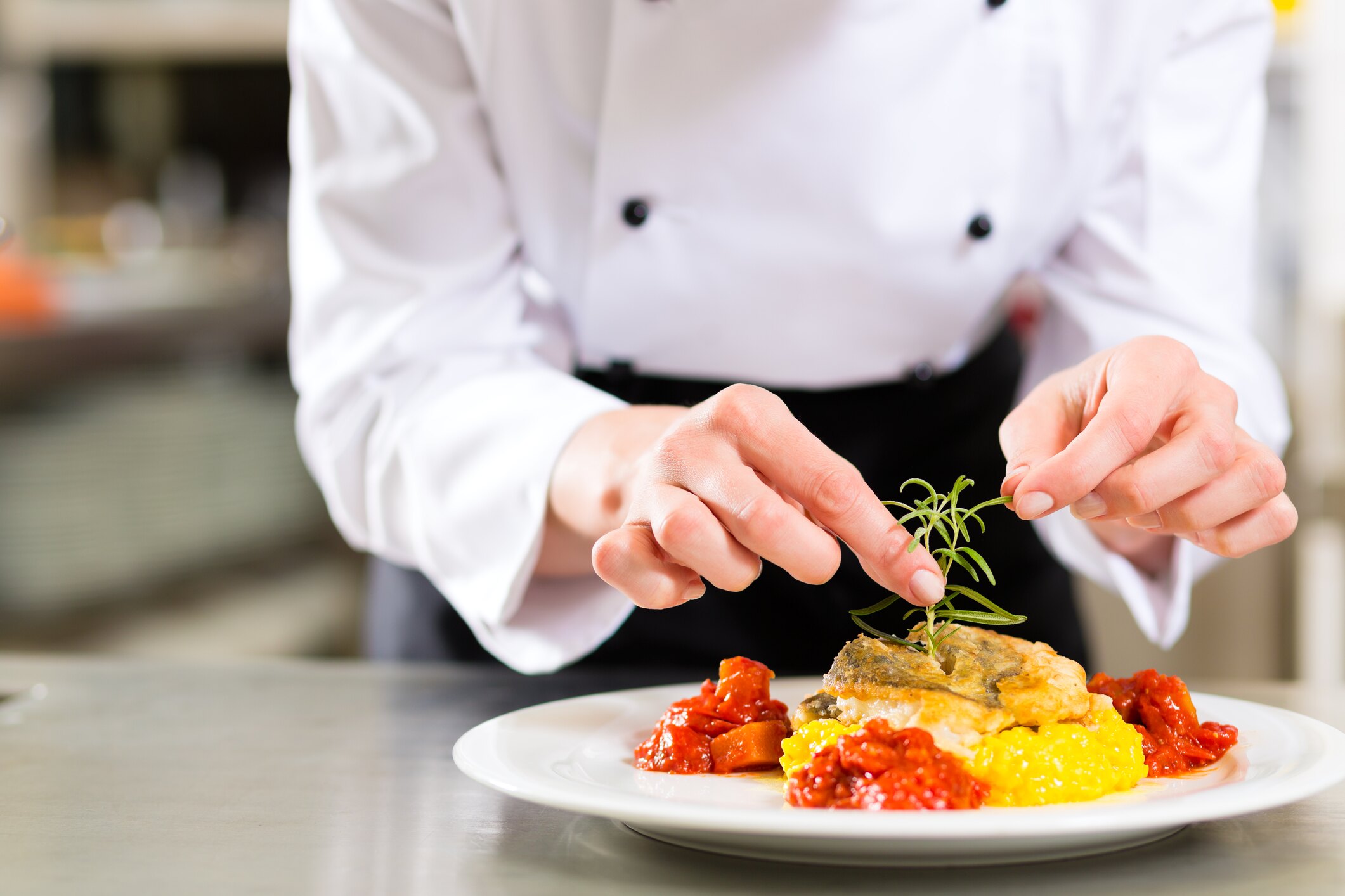 A chef in whites placing a sprig of herb on a plated fish