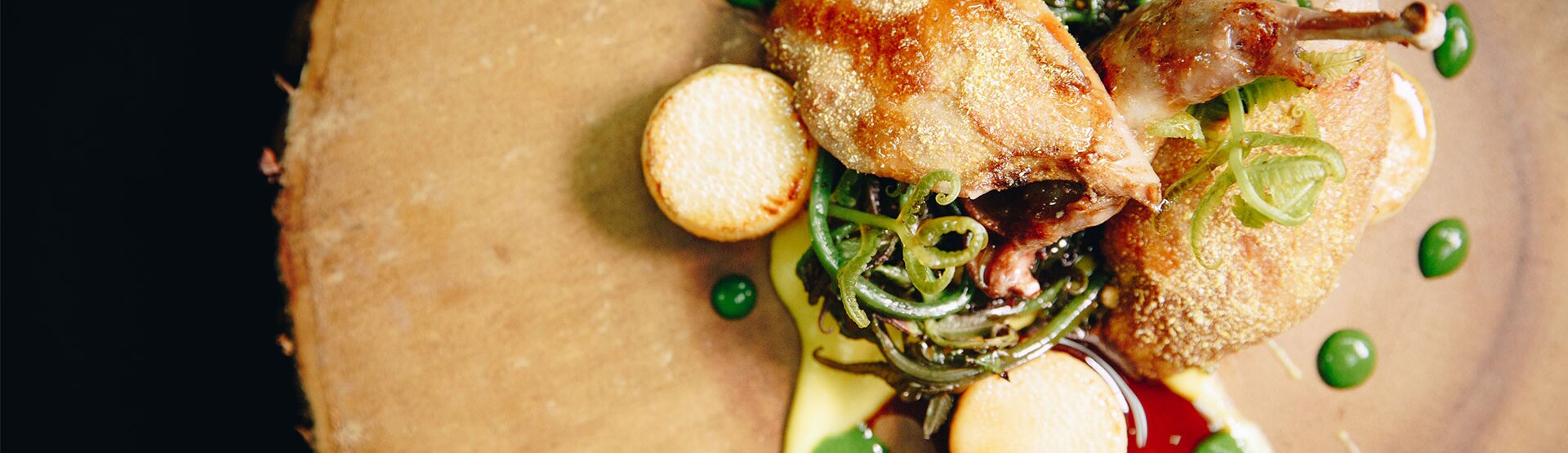 A plated dish from above — crisp-skinned bird, green shoots and pea purée on a wooden board