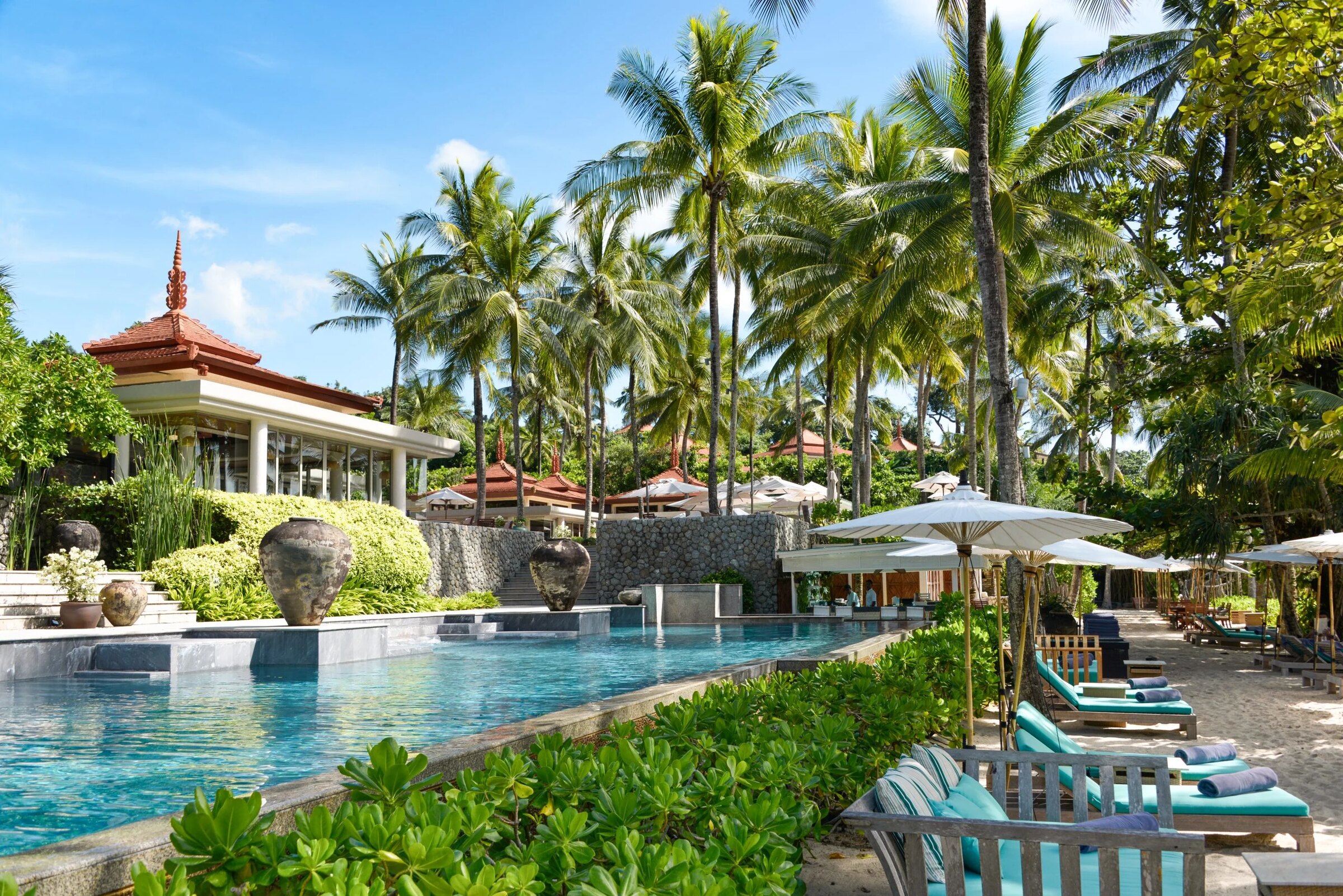 Trisara's pool and teak loungers under coconut palms, a red-roofed pavilion behind, Phuket