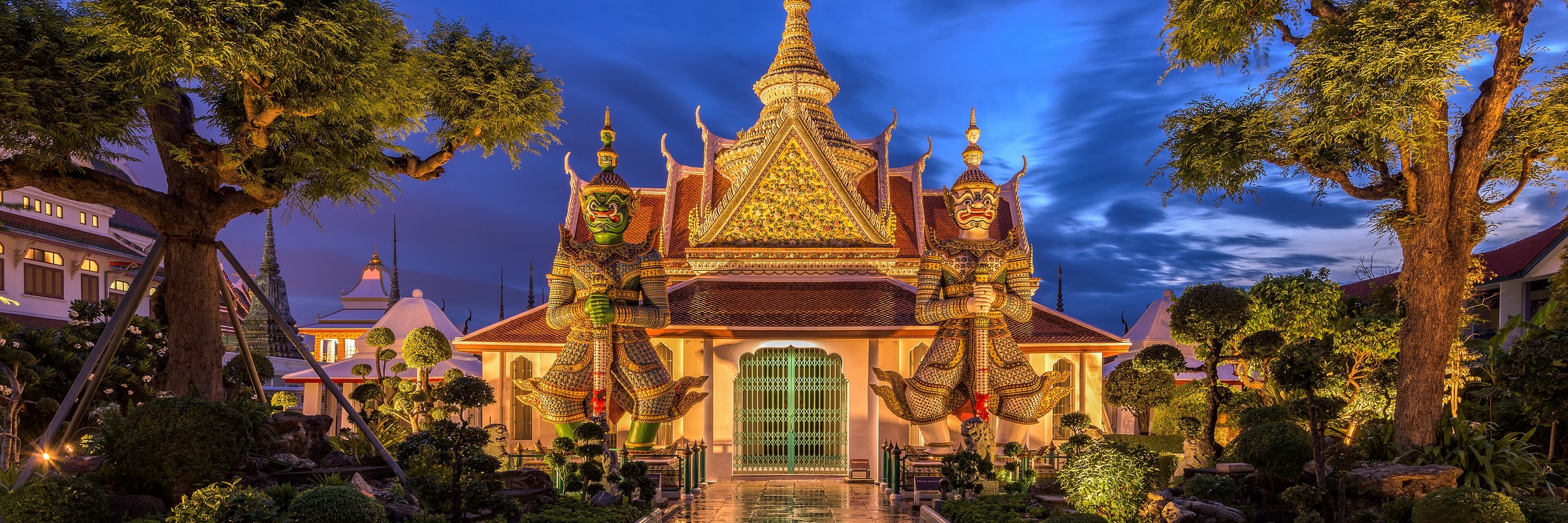 Guardian giants before an illuminated temple hall at blue hour, Bangkok